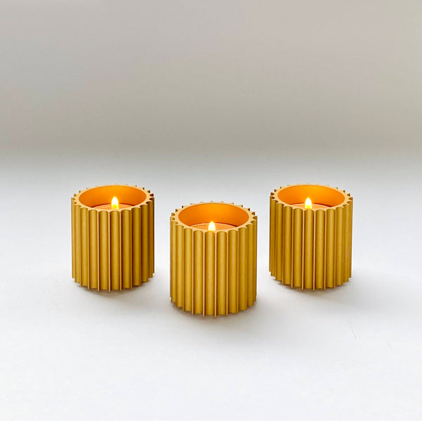 A set of three gold anodized aluminum candle holders with fluted designs, designed to hold tea lights or similar sized candles.