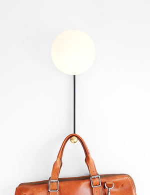Hook Sconce is a wall light with integrated hook holding a leather satchel