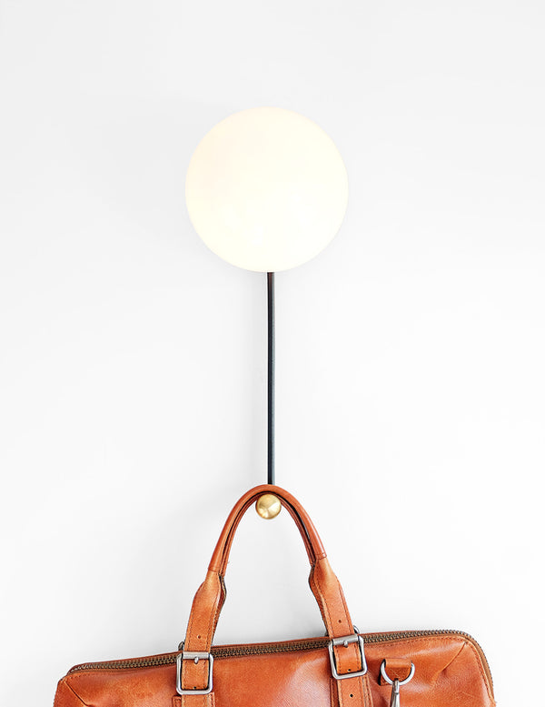 Hook Sconce is a wall light with integrated hook holding a leather satchel